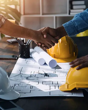 Two men shaking hands over construction plans